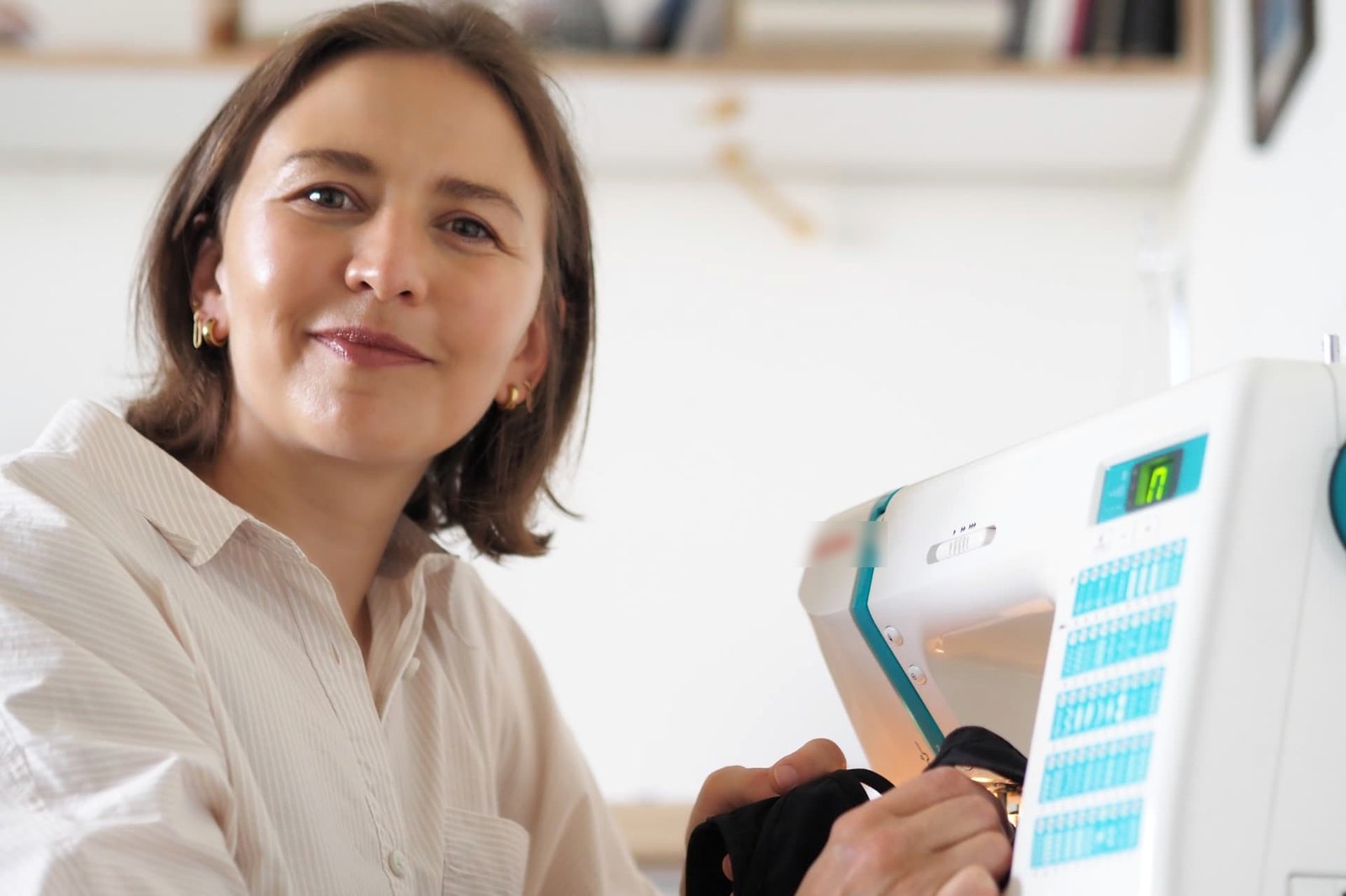 Belgian lingerie designer Els smiling at her sewing machine while stitching black fabric for the Vicky Baey Essential Tucking Thong.