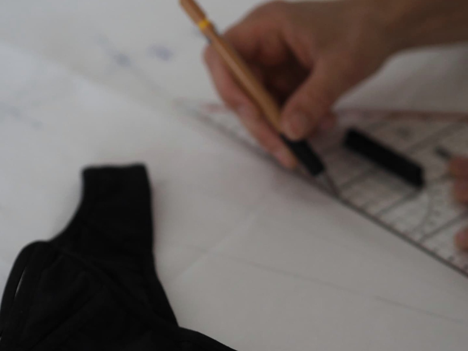 Design details of the Vicky Baey Essential Tucking Thong: a pencil and ruler on pattern paper beside the black thong on the studio table.