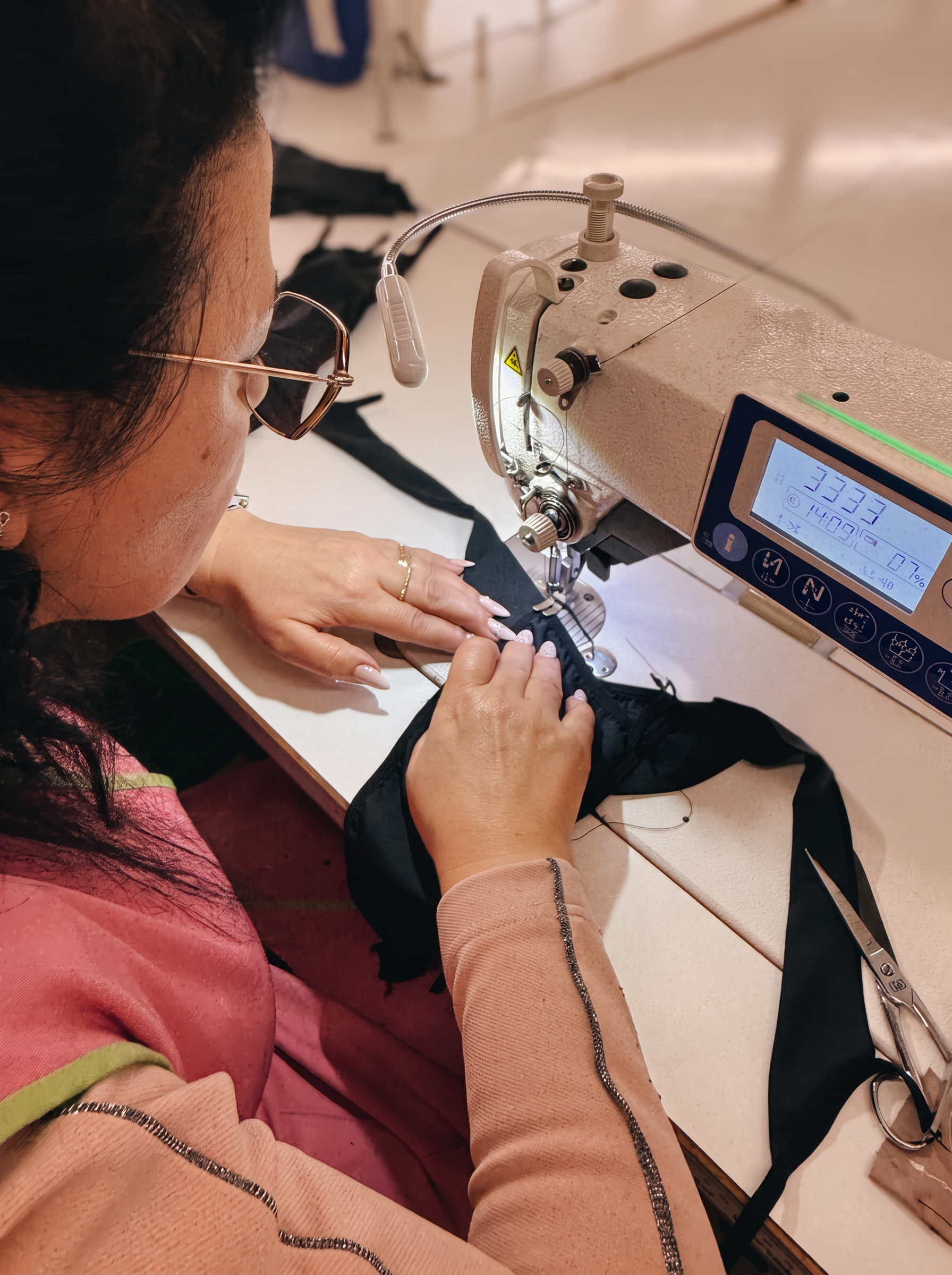 A seamstress in our Portuguese atelier sewing black lingerie on an industrial machine, guiding the fabric with careful hands, warm workshop light.